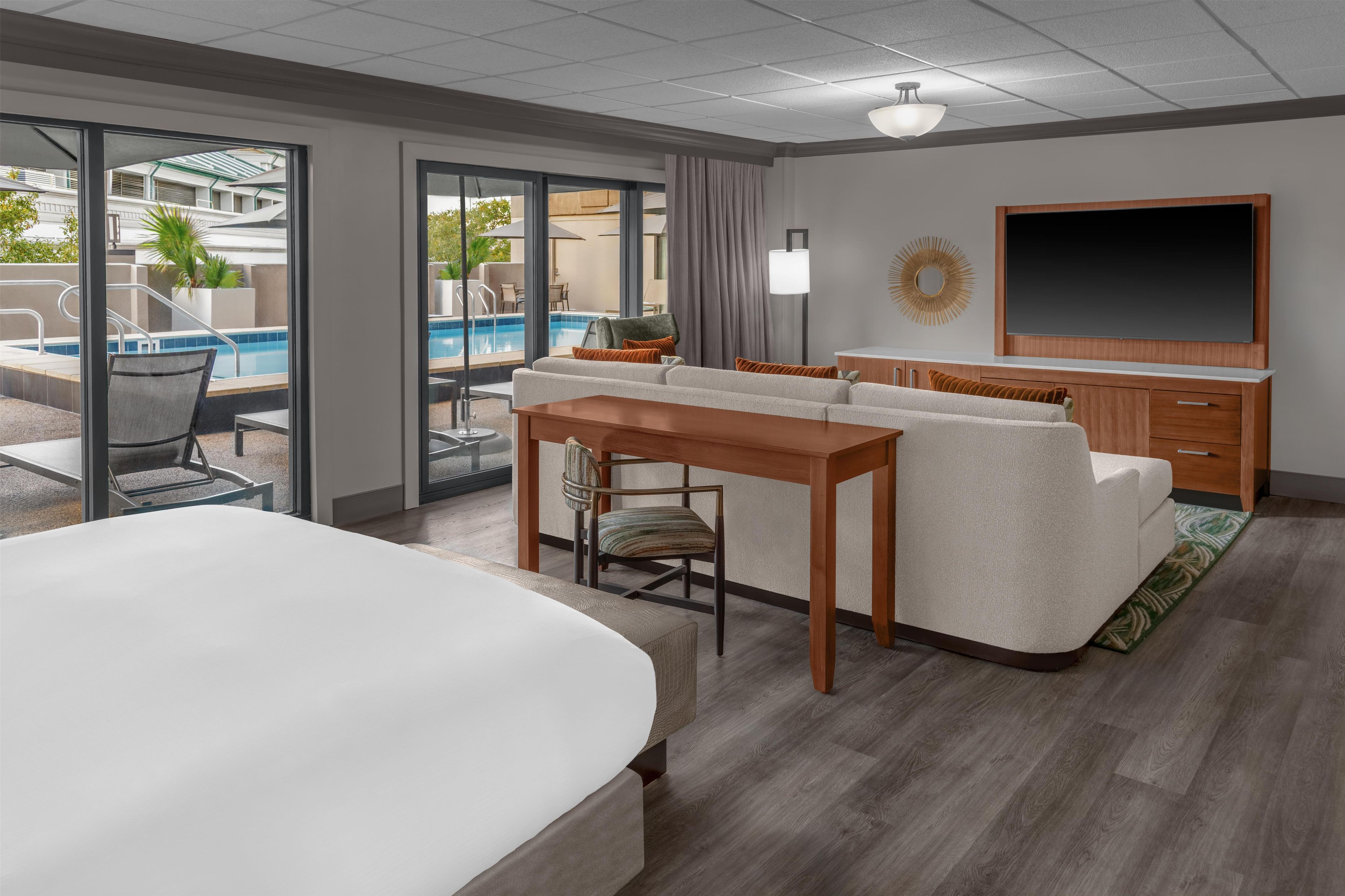 Une chambre d’hôtel avec un grand lit, un canapé, une table à manger, une télévision et une vue sur une piscine.