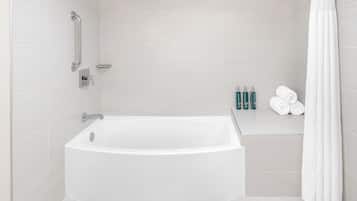 A modern bathroom with a white bathtub, a shower with a handheld showerhead, and a grab bar. There are toiletries on the wall and towels on a shelf.
