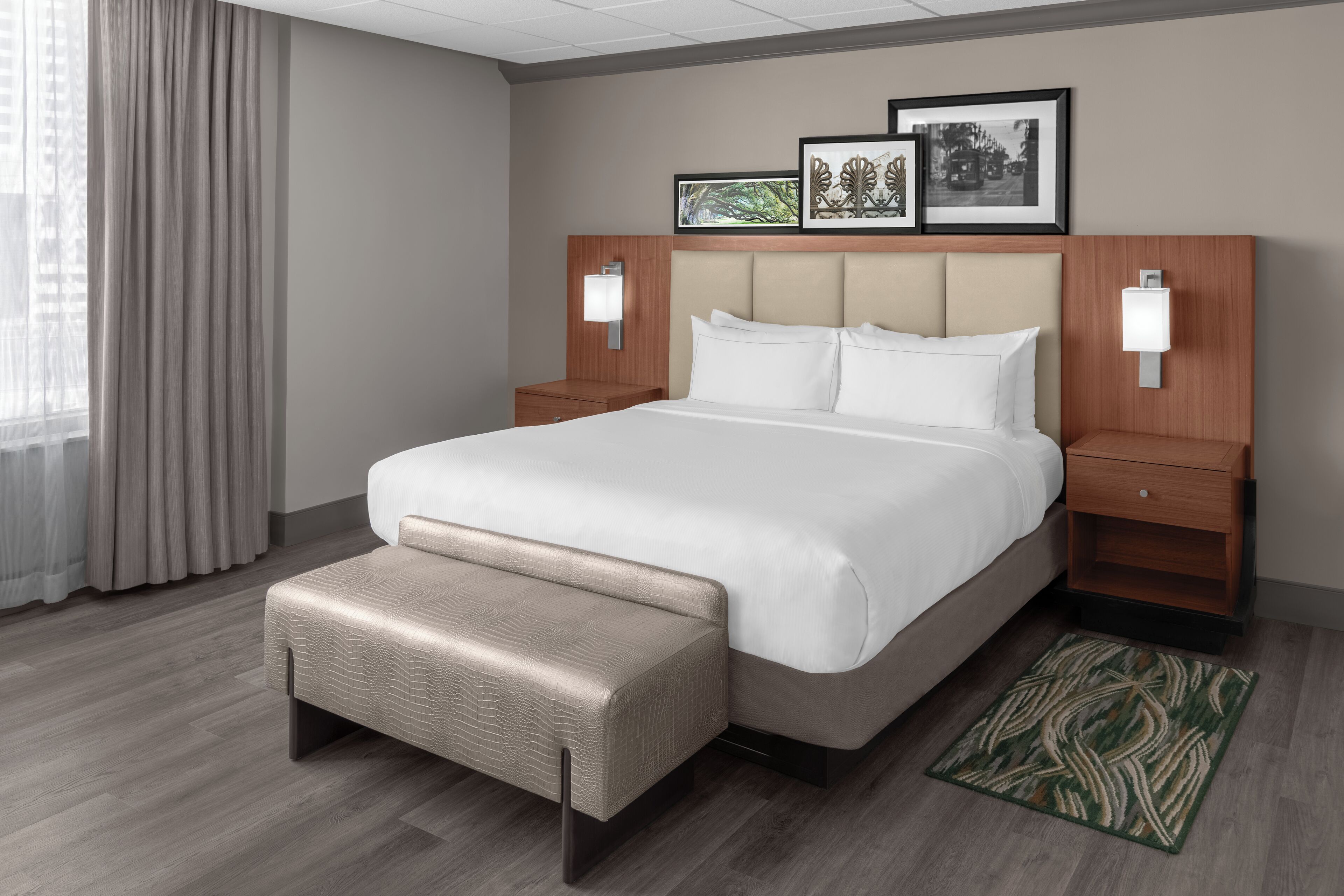 A hotel room with a large bed, a bench, two bedside tables, and a headboard with wall-mounted lamps.