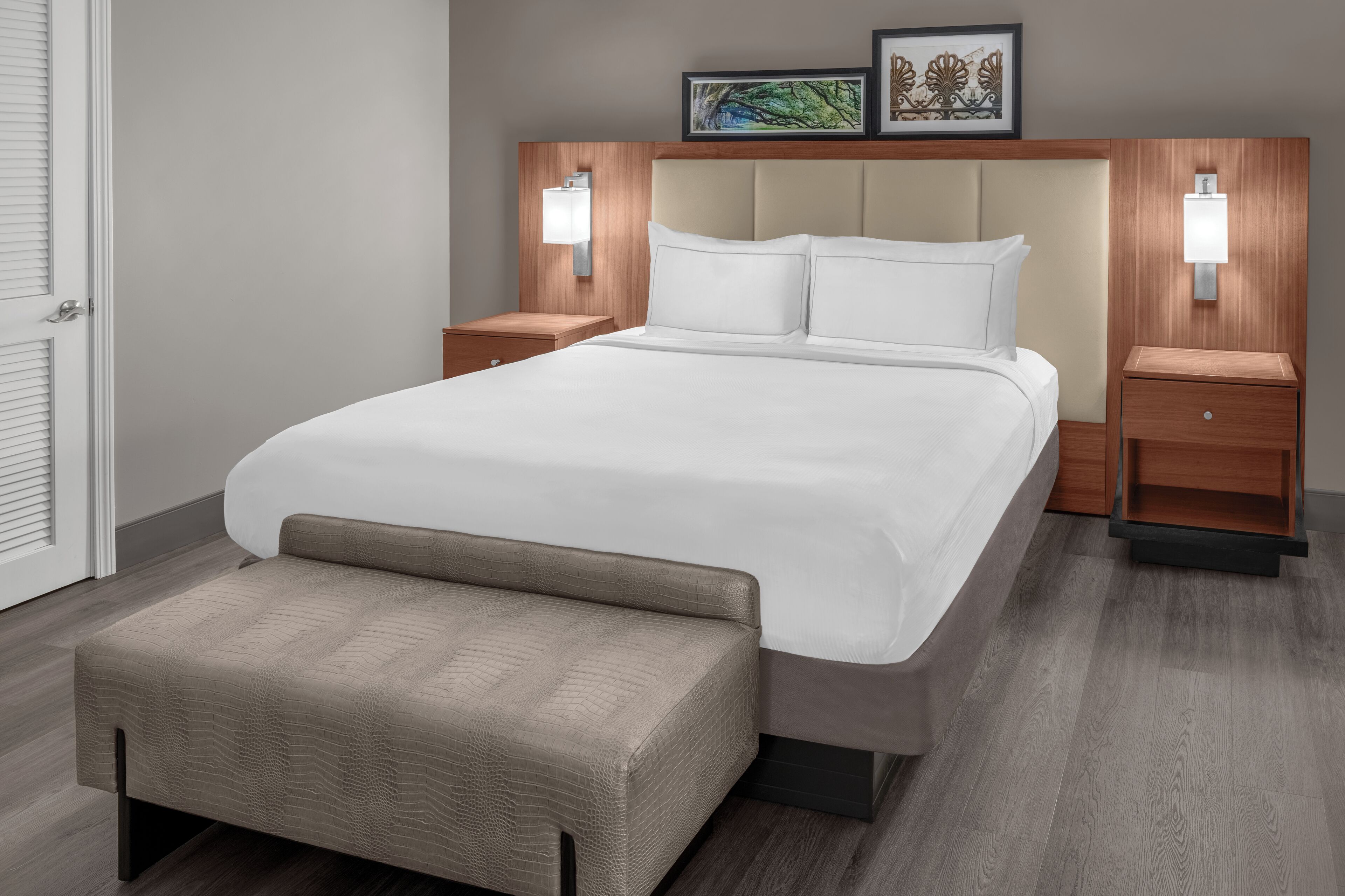 A modern hotel room with a large bed, two bedside tables, a bench, and wall-mounted lights.