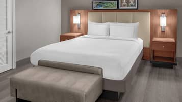 Una habitación de hotel moderna con una cama grande, dos mesitas de noche, un banco y luces fijadas a la pared.
