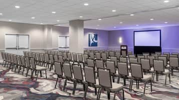 A conference room with rows of chairs, a projector screen, and a large abstract painting on the wall.
