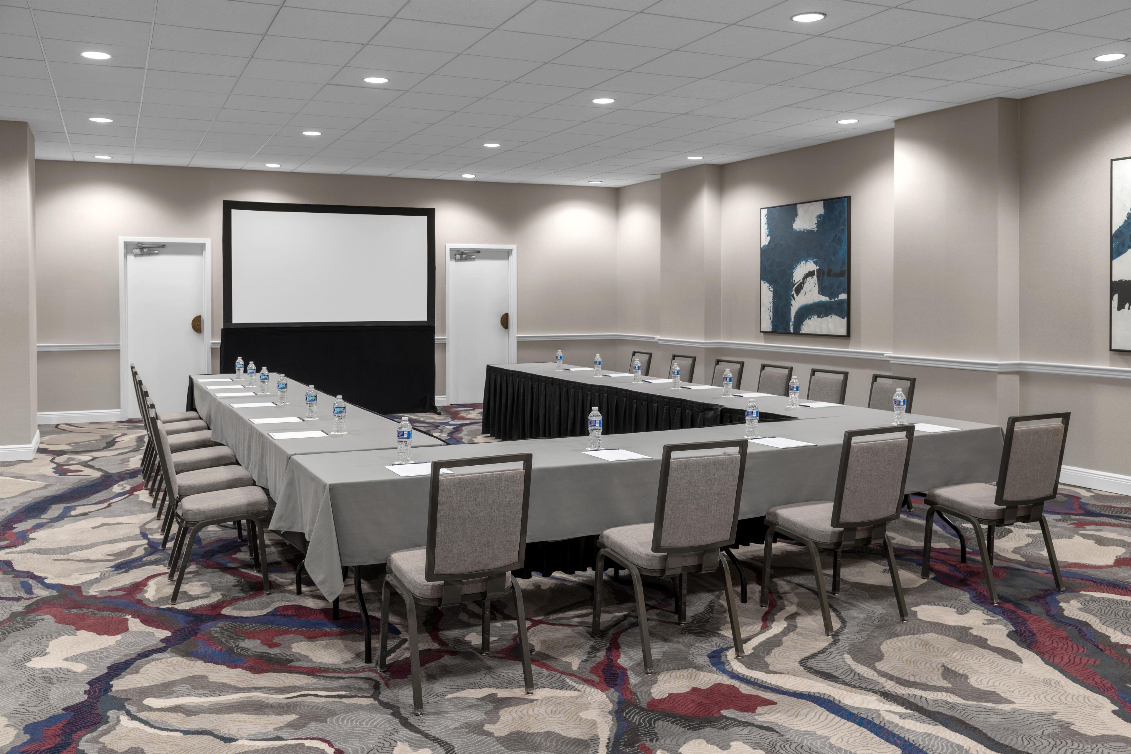 A conference room with a long table, chairs, a projector screen, and a water bottle on the table.
