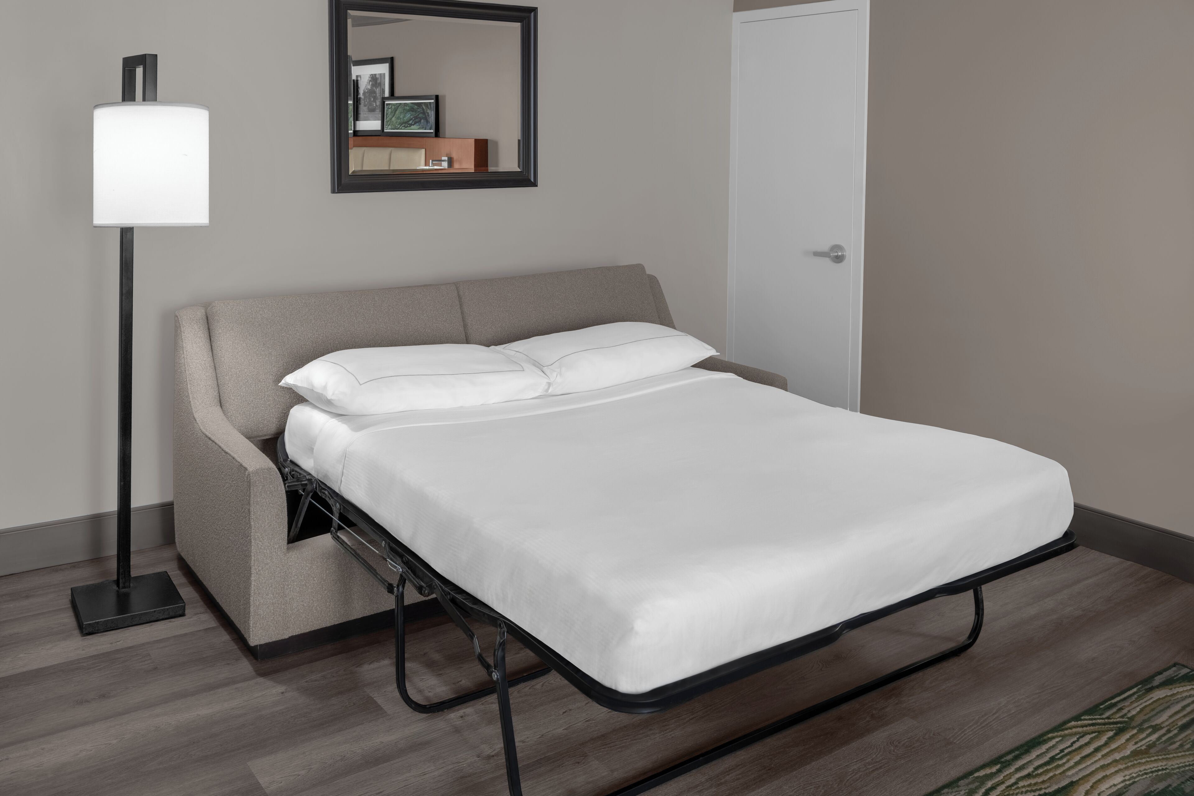 Un dormitorio moderno con cama, lámpara de pie, espejo y puerta.