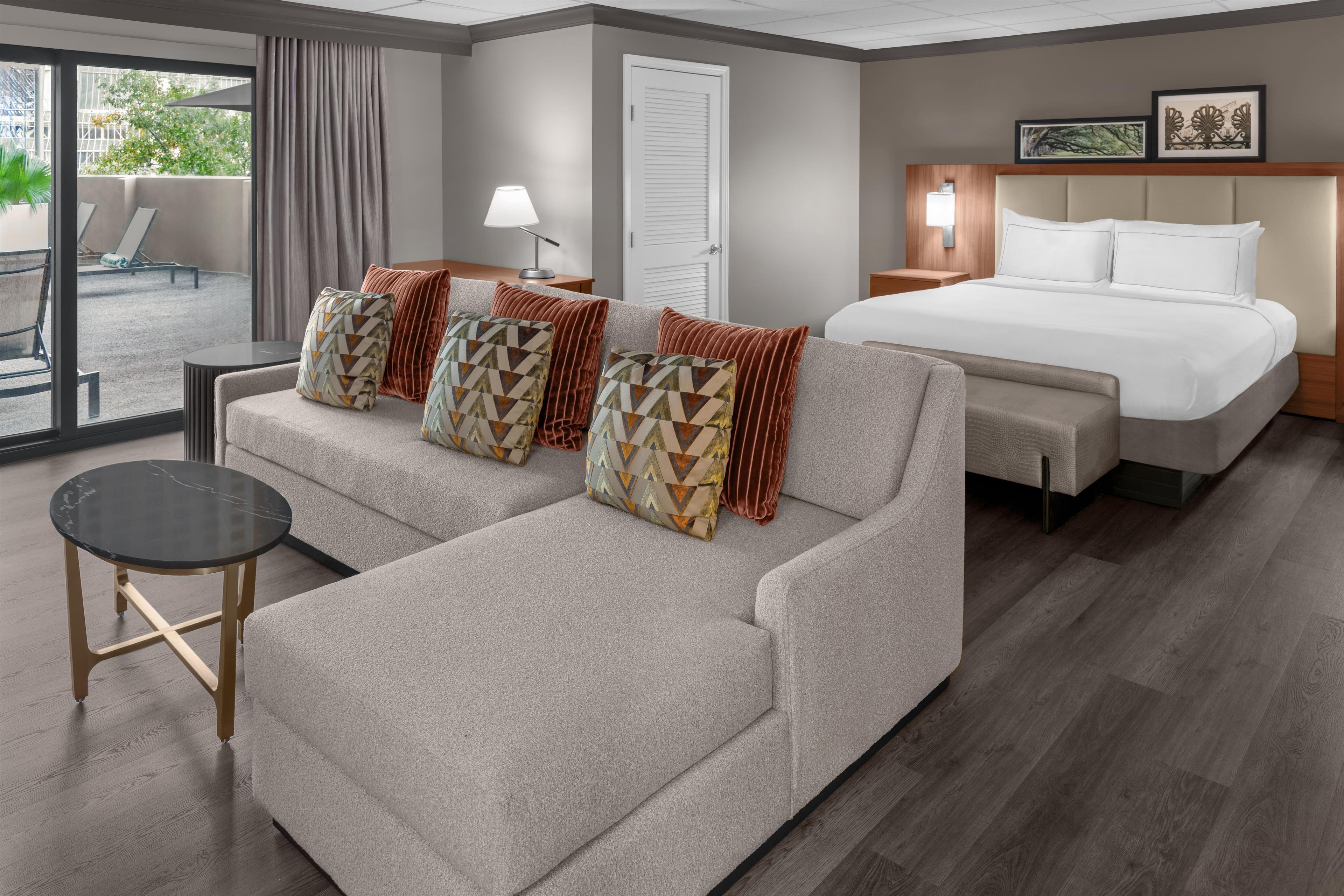 A hotel room with a sofa, a bed, a small table, and a view of the outdoors.
