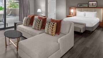 A hotel room with a sofa, a bed, a small table, and a view of the outdoors.