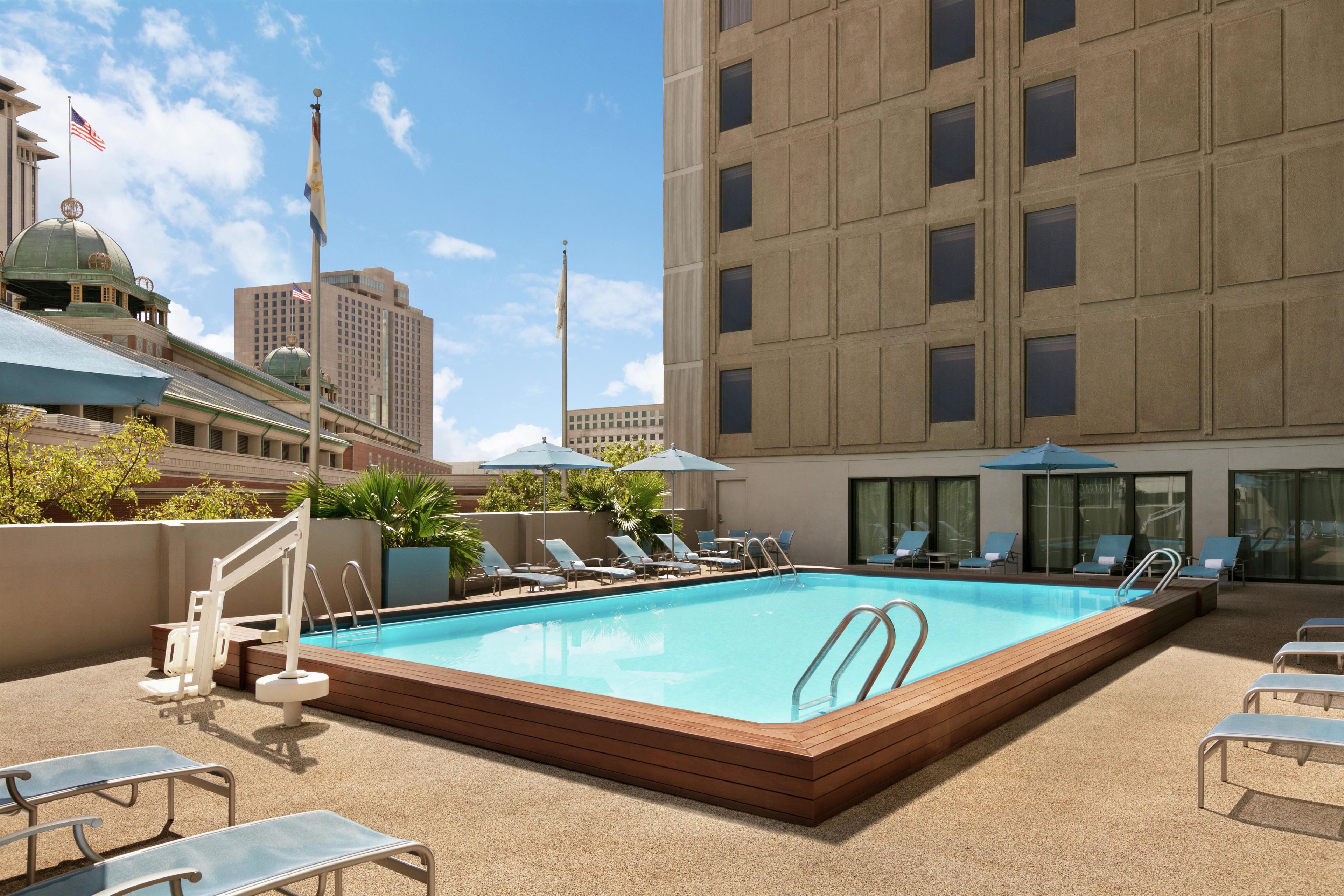 A rooftop pool area with lounge chairs, umbrellas, and a view of the cityscape.