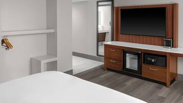 A modern hotel room with a large bed, a wooden desk with a flat-screen TV, a built-in microwave, and a small refrigerator.