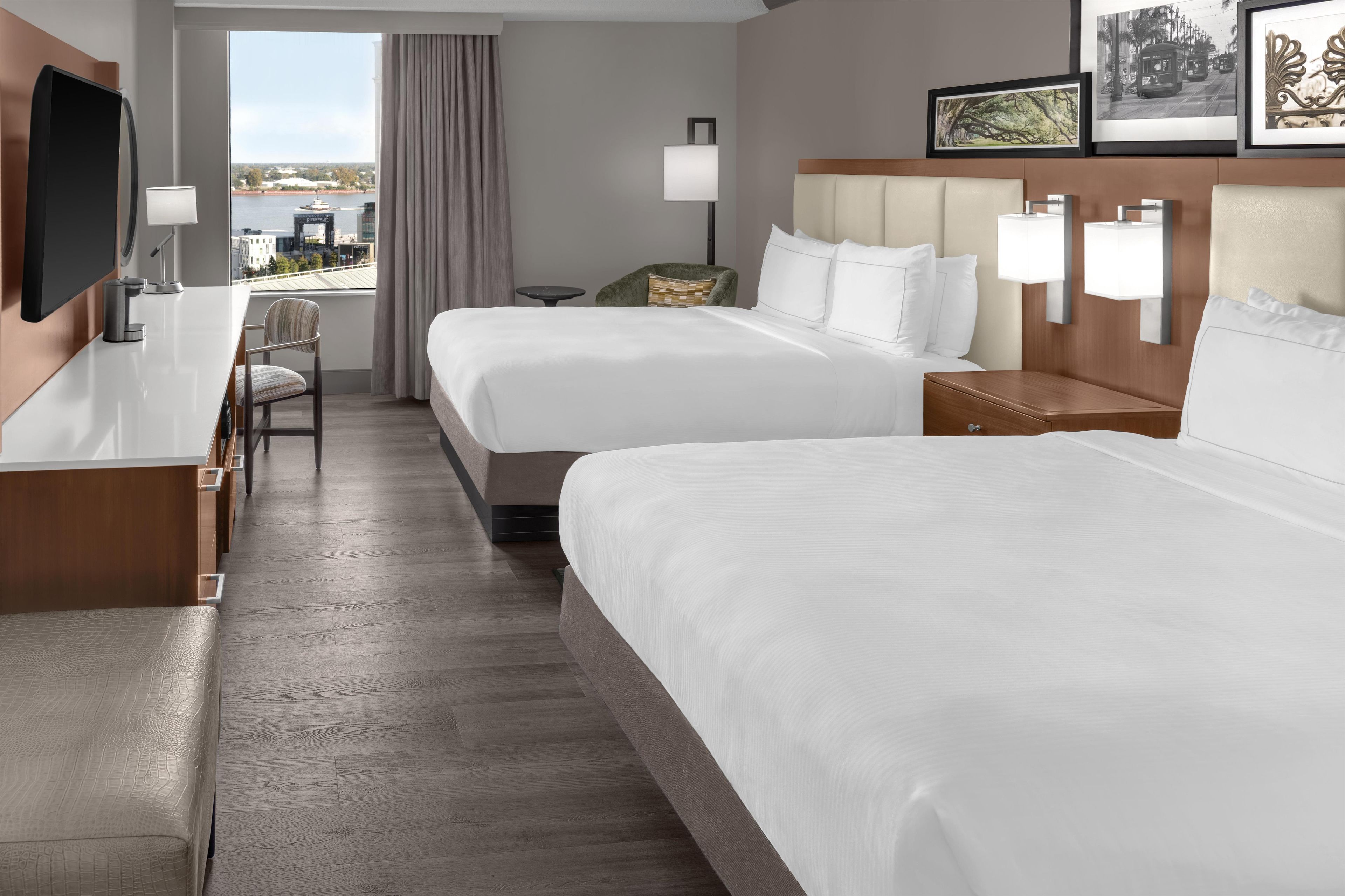 A hotel room with two beds, a desk, a chair, and a TV.