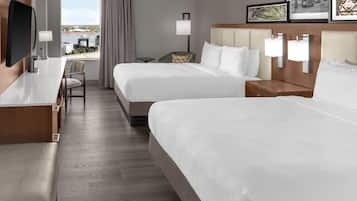 A hotel room with two beds, a desk, a chair, and a TV.