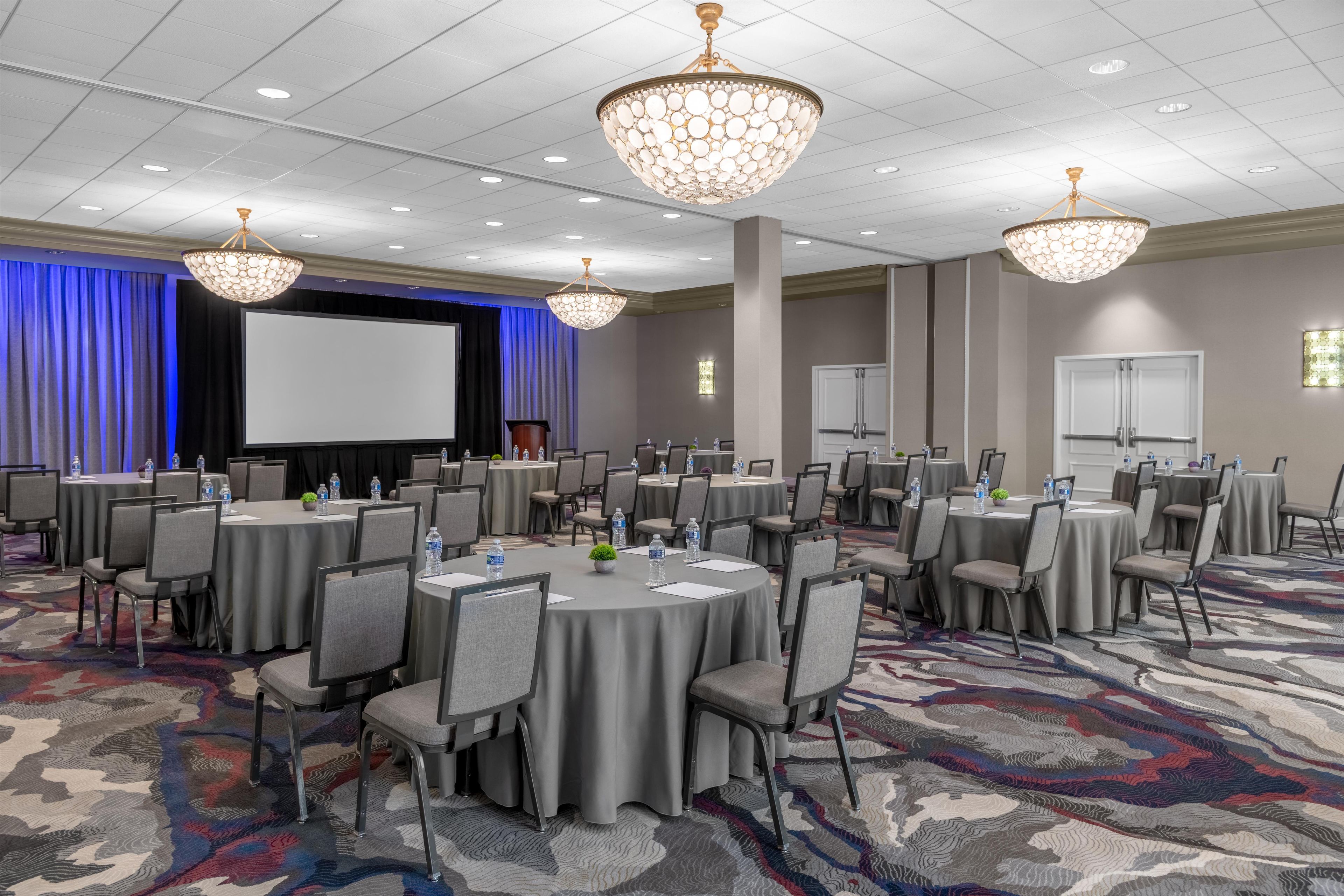 A conference room with round tables, chairs, and a large screen.