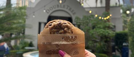 A hand holding a cookie bag with a logo, in front of a building with a sign that reads "DOUBLETREE".