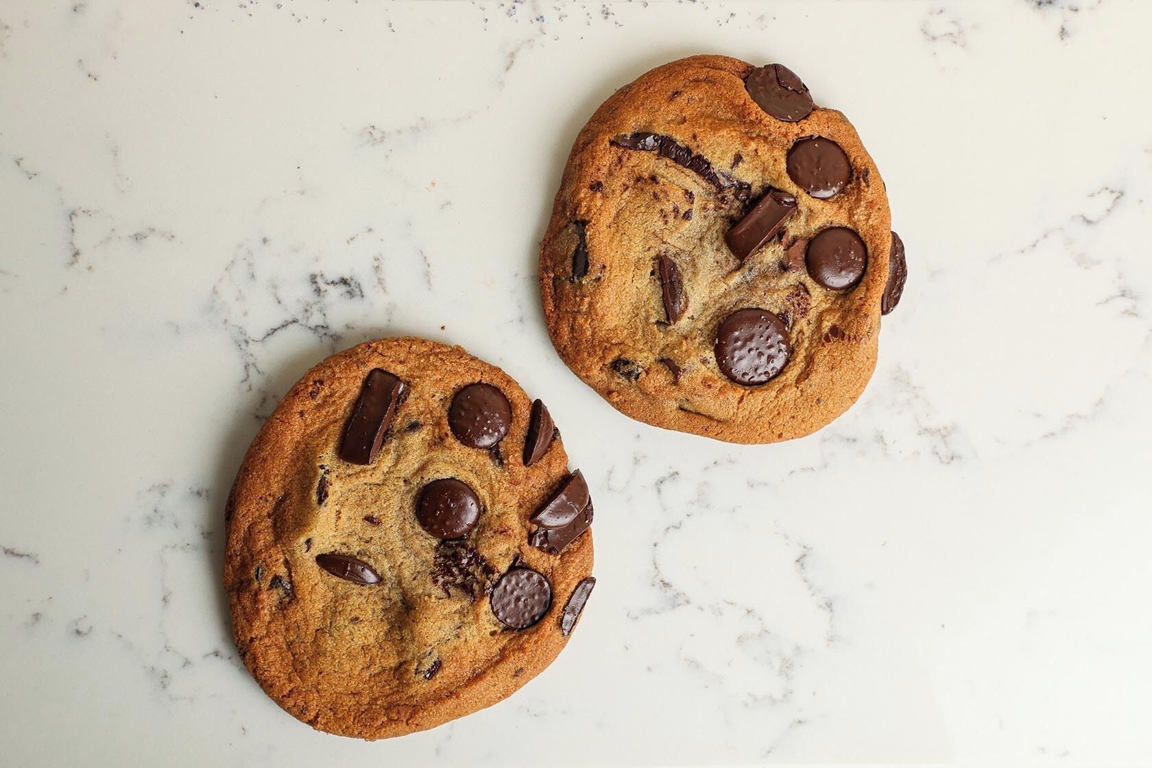 Two chocolate chip cookies on a marble surface.