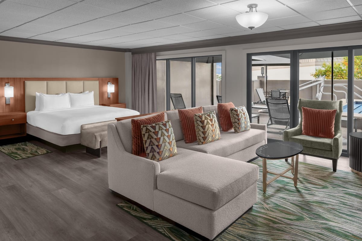 A hotel room with a bed, a sofa, a small table, and a view of the outside.