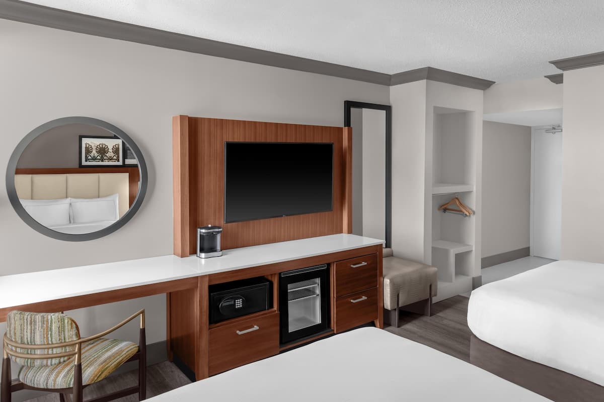 A hotel room with a wooden desk, a minibar, a TV, a bed, a chair, and a walk-in closet.