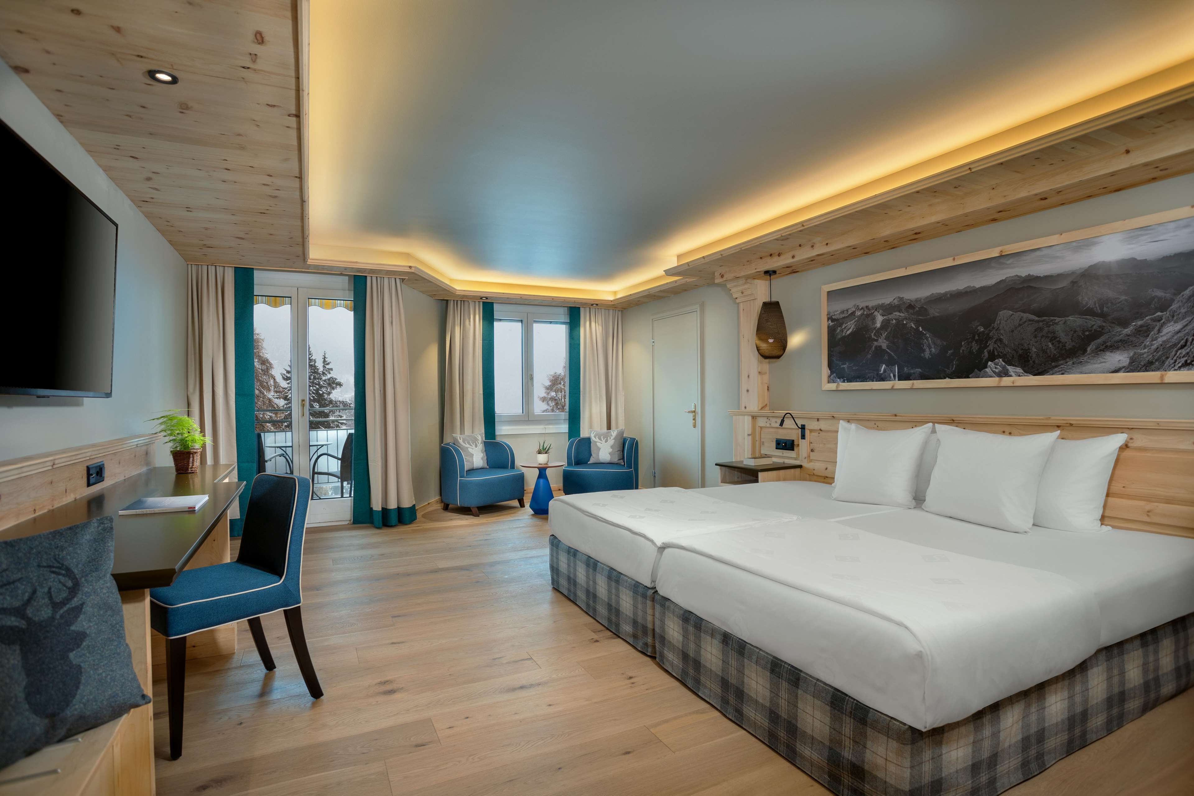 A modern hotel room with a large bed, a desk with a chair, a TV, and a painting on the wall.