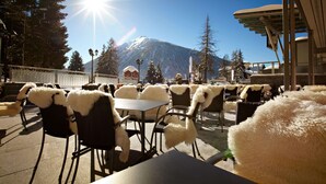 An outdoor café with tables and chairs, a mountain in the background, and a clear sky.