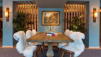 A dining area with a wooden table, white furry chairs, and a framed painting on the wall.