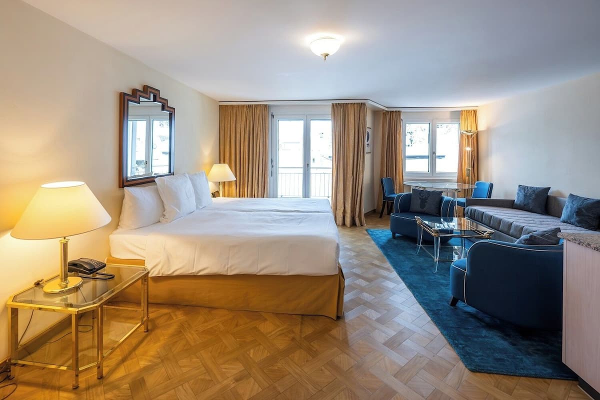 A hotel room with a large bed, a sofa, a small table, and a desk with a lamp.
