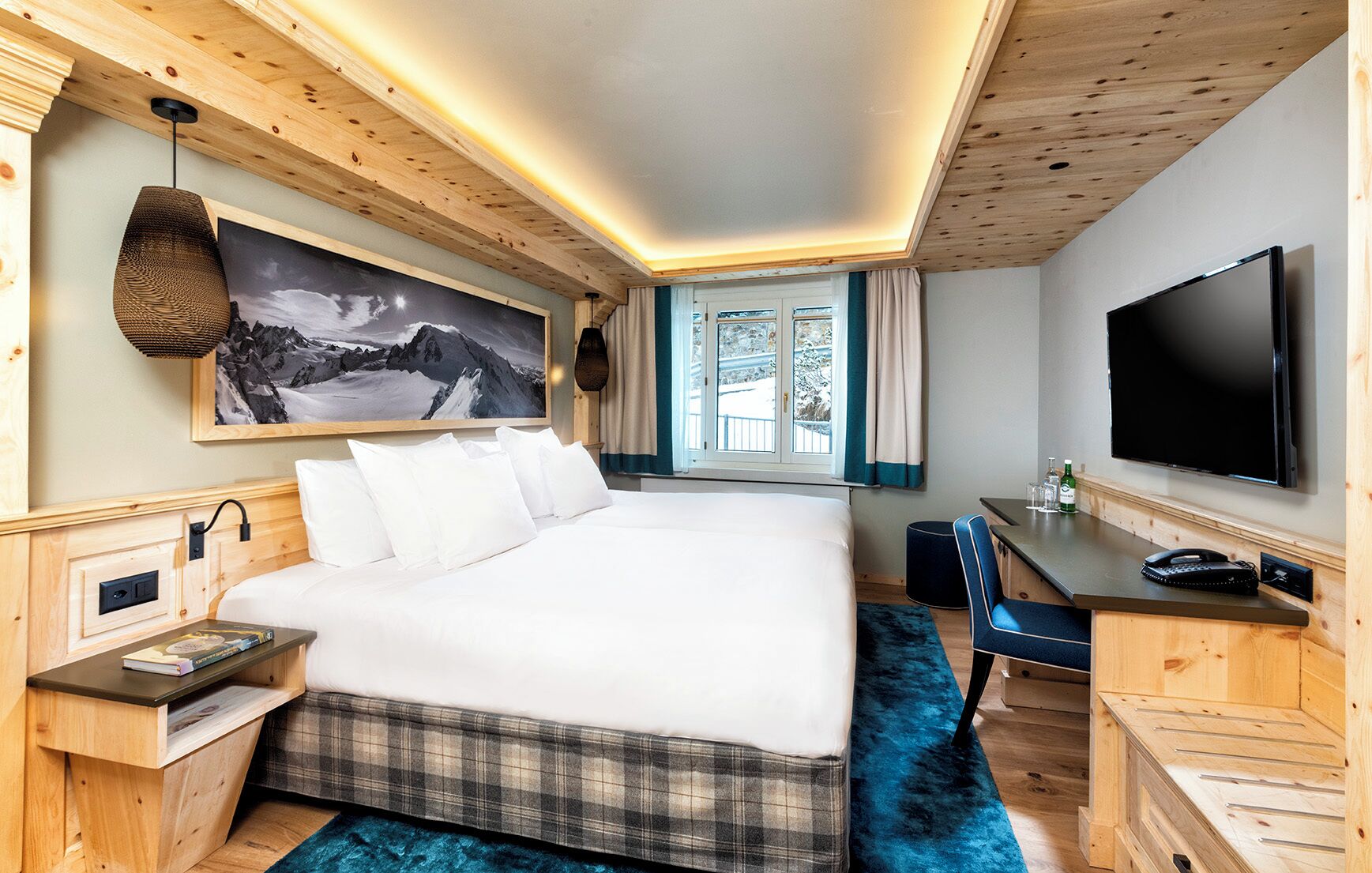 A hotel room with a bed, a desk, a television, and a window with curtains.