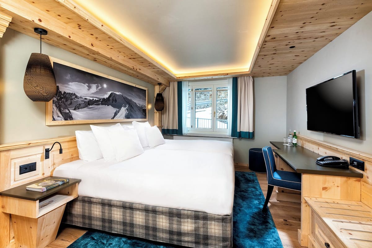 A hotel room with a bed, a desk, a television, and a window with curtains.