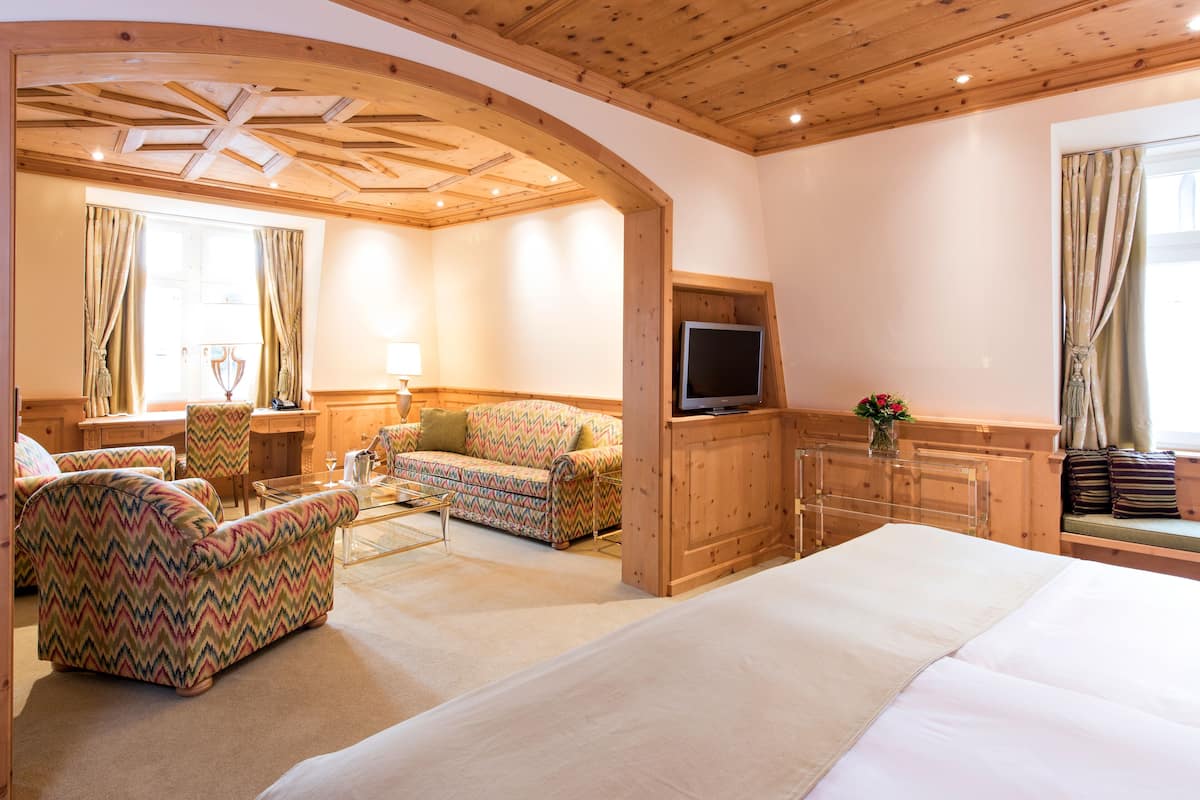 A hotel room with a large bed, a sofa, a TV, and a wooden ceiling.