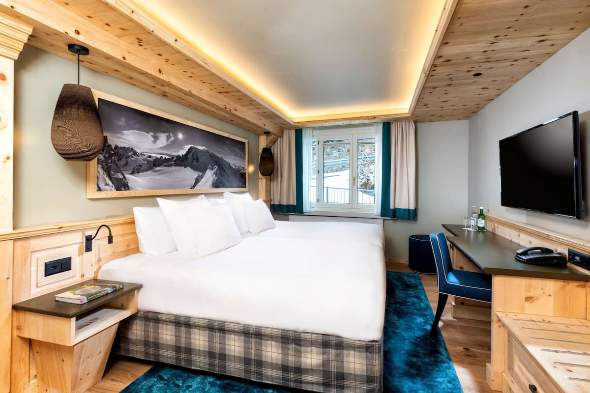 A modern hotel room with a large bed, a desk, a TV, and a mountain landscape painting.
