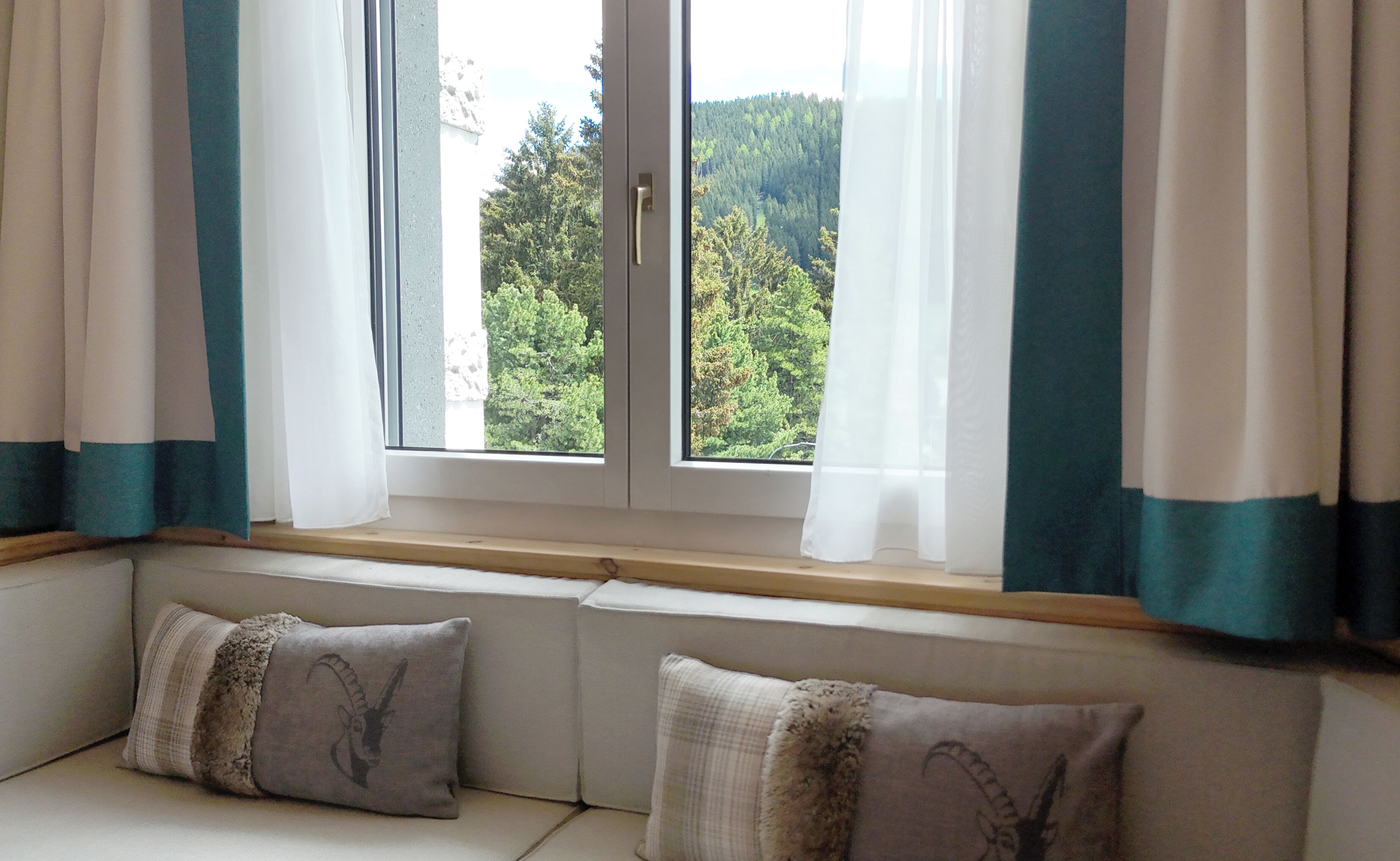 A room with a large window, a bench with cushions, and a view of a forested area.