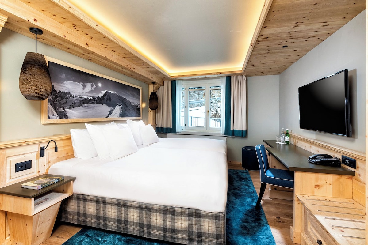 A hotel room with a bed, a desk, a television, and a window with curtains.
