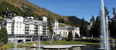 A hotel with multiple floors, a fountain, and a lake in the foreground.