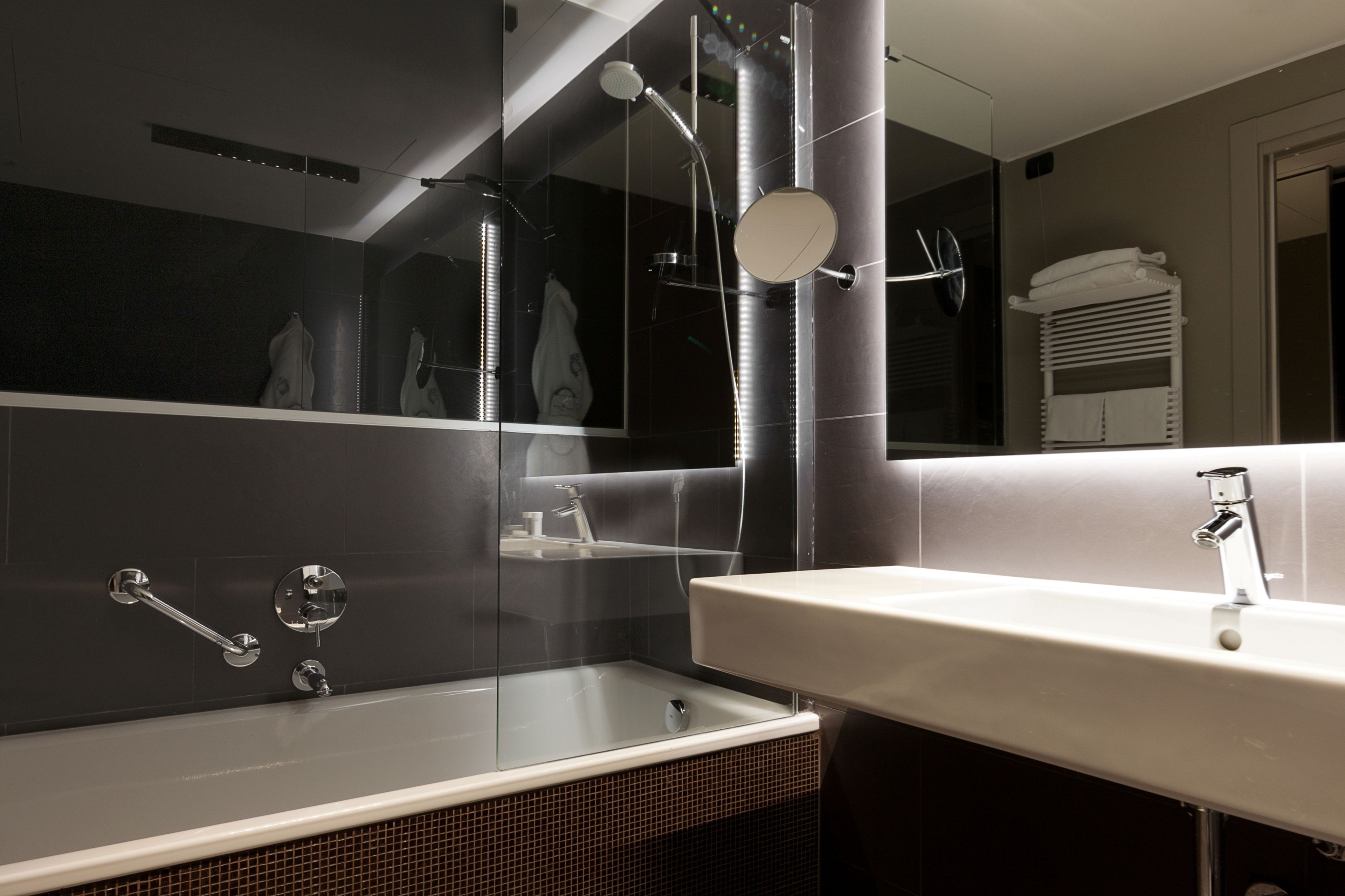 A modern bathroom with a glass-enclosed shower, a white sink, and a towel rack.