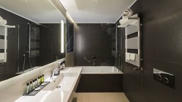 Een moderne badkamer met een grote spiegel, een badkuip, een douche en een wastafel met toiletartikelen.