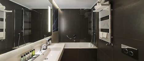 Un baño moderno con un espejo grande, una bañera, una ducha y un lavabo con artículos de aseo.