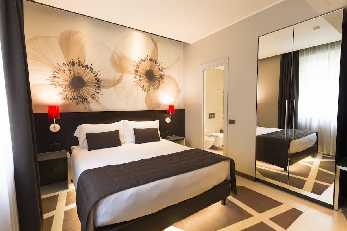Une chambre d’hôtel moderne avec un grand lit, un miroir et un mur décoré d’œuvres d’art florales.