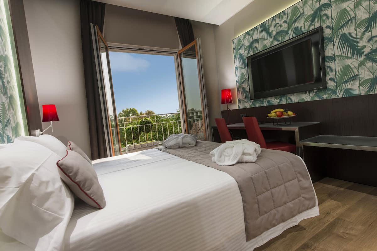 Une chambre d’hôtel avec un lit, un bureau, une télévision et un balcon offrant une vue.