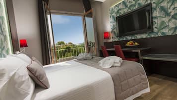 Een hotelkamer met een bed, een bureau, een televisie en een balkon met uitzicht.