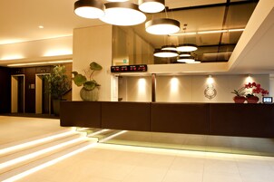 Una moderna area reception con orologio digitale che mostra informazioni sui voli, una scrivania reception e una scala che conduce a un piano superiore.