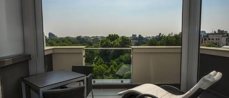 Un balcon avec une table et des chaises, un fauteuil confortable et une vue sur le paysage urbain, agrémenté de verdure.