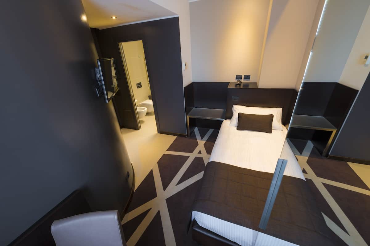 Une chambre d’hôtel moderne, dotée d’un grand lit, d’une table de chevet, d’une chaise et d’une salle de bain visible à travers une porte ouverte.