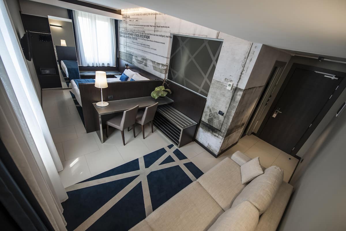 Une chambre d’hôtel moderne, équipée d’un canapé, d’un bureau avec une lampe, d’une petite table et offrant une vue sur la ville.