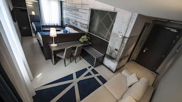 Een moderne hotelkamer met een bank, een bureau met een lamp, een klein tafeltje en uitzicht op de stad.