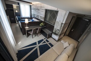 Een moderne hotelkamer met een bank, een bureau met een lamp, een klein tafeltje en uitzicht op de stad.
