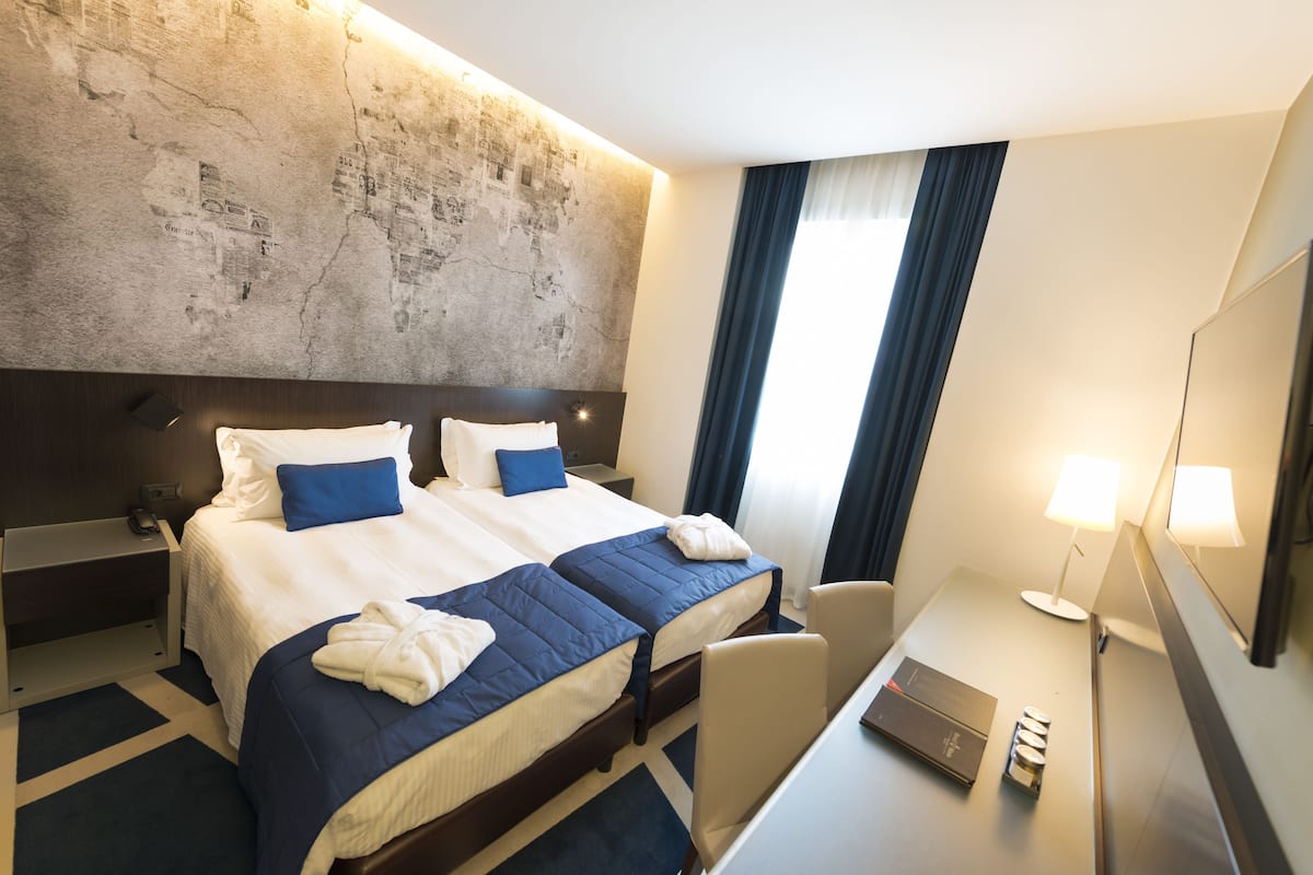 Une chambre d’hôtel avec deux lits, un bureau, une chaise, une lampe et un grand miroir.