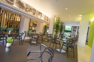 A modern indoor dining area with multiple tables and chairs, potted plants, and a high ceiling with recessed lighting.