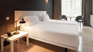 A hotel room with a large bed, bedside table with a lamp, and a chair near a window with curtains. - Sercotel Togumar (Madrid)