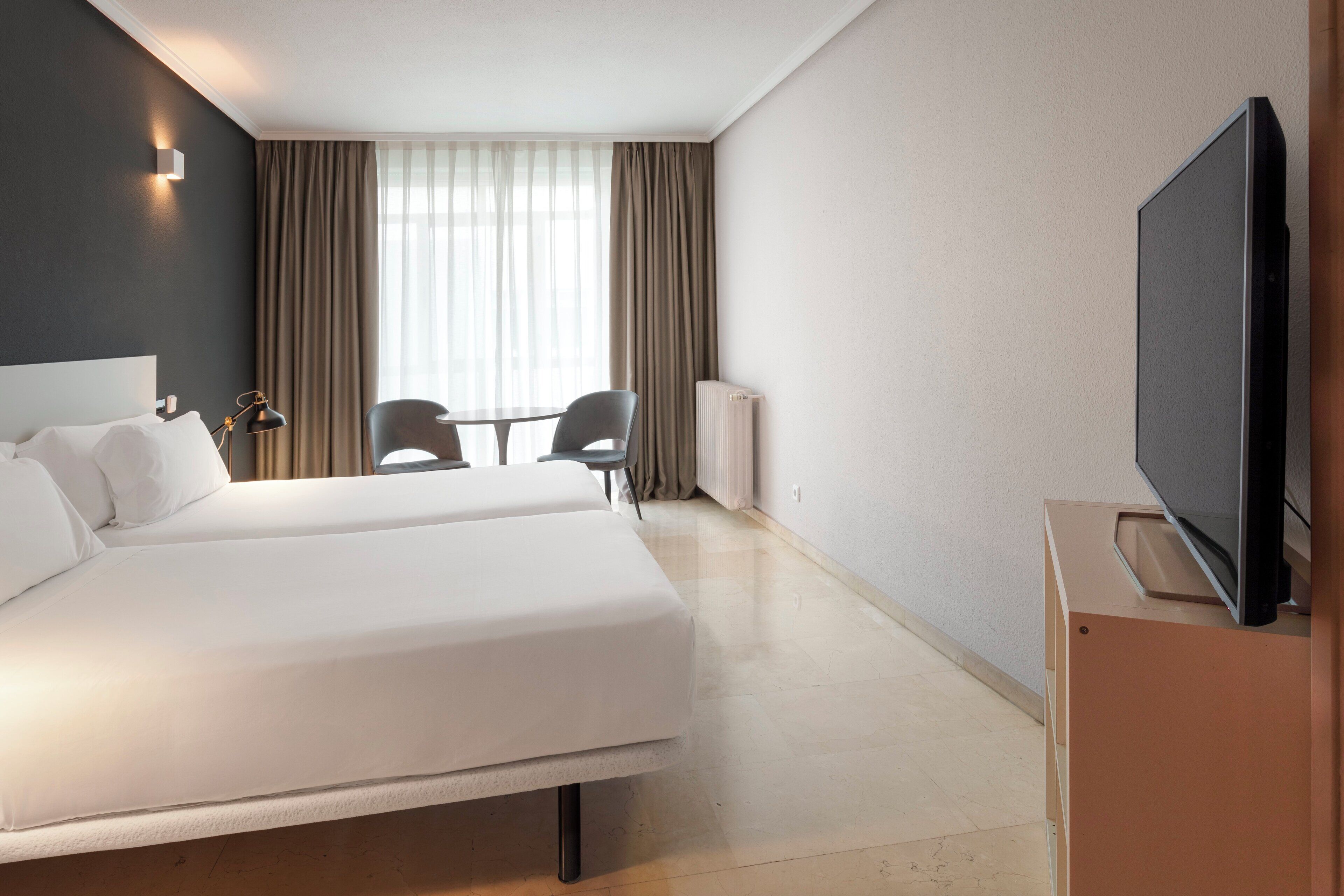 Een hotelkamer met twee bedden, een televisie, een tafel met stoelen en een raam met gordijnen.