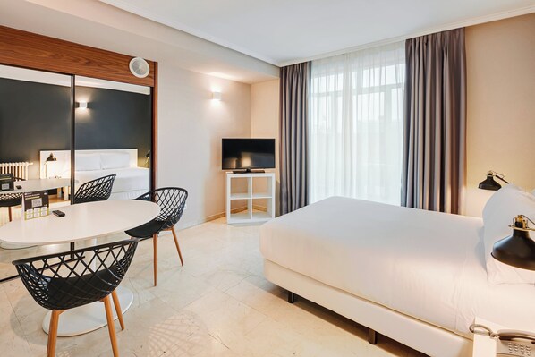 A hotel room with a bed, a TV, a dining table with chairs, and a small cabinet. - Sercotel Togumar (Madrid)