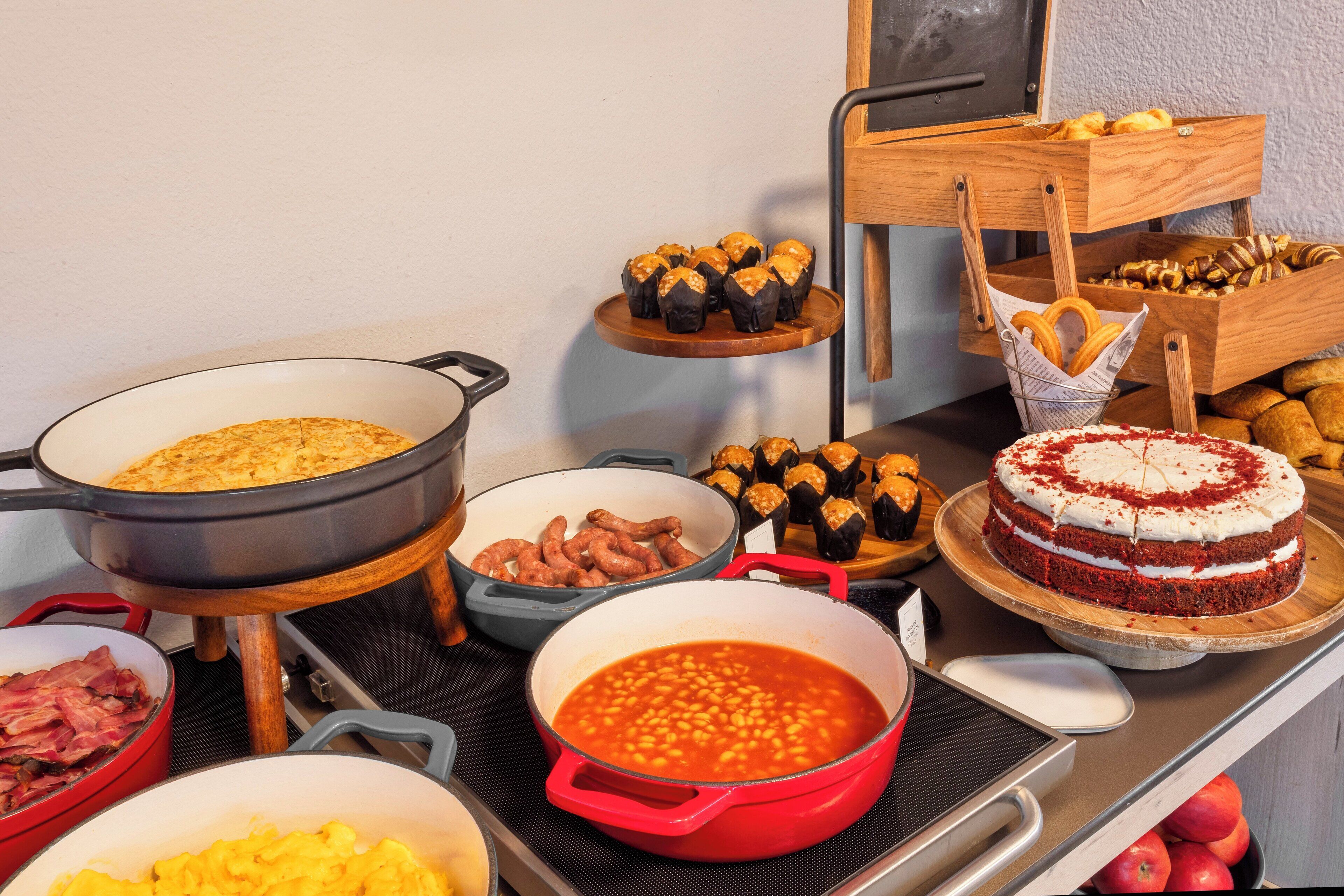 A buffet table with various dishes including baked goods, a cake, and a pot of beans.