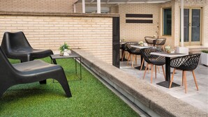 A patio area with a brick wall, a small table with chairs, and a covered seating area. - Sercotel Togumar (Madrid)