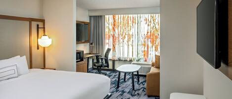 Habitación de hotel con una cama grande, un escritorio, televisión y vistas a hojas otoñales por la ventana.